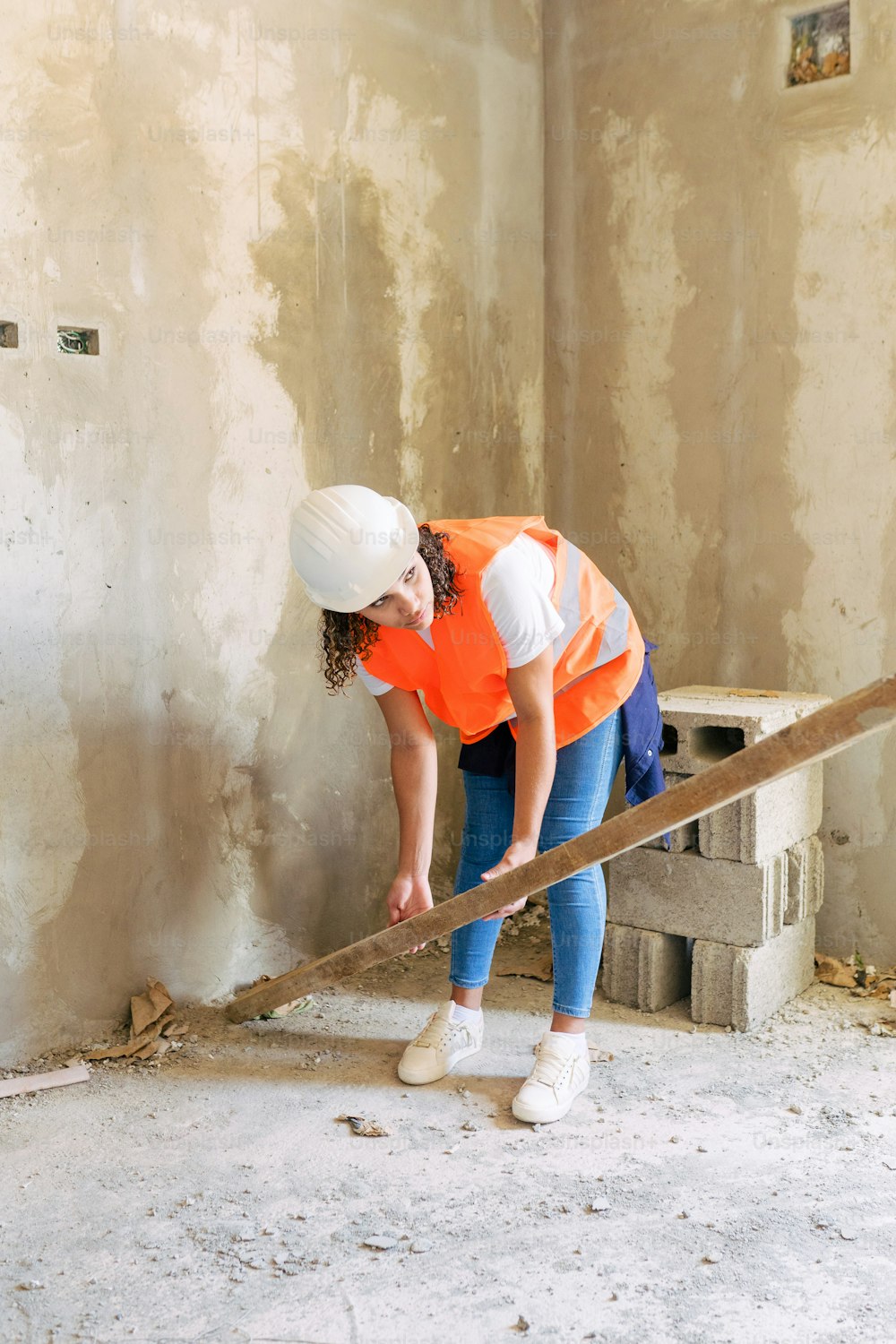 a woman in an orange vest and white hat working on a wall