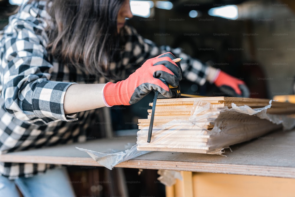 a woman in a plaid shirt and gloves working on a piece of wood