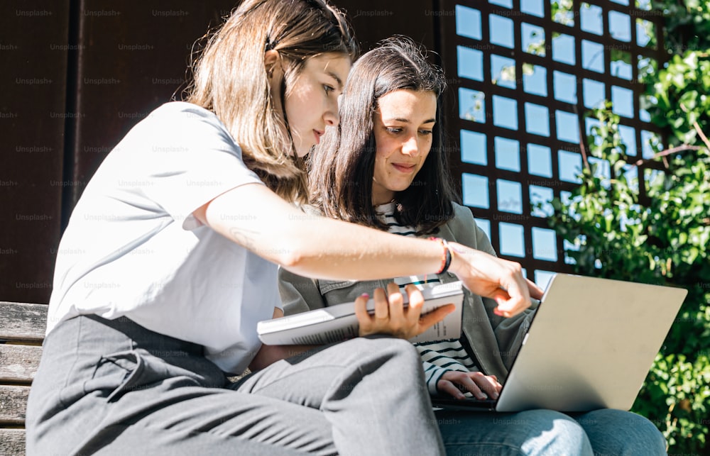 two women sitting on a bench looking at a laptop