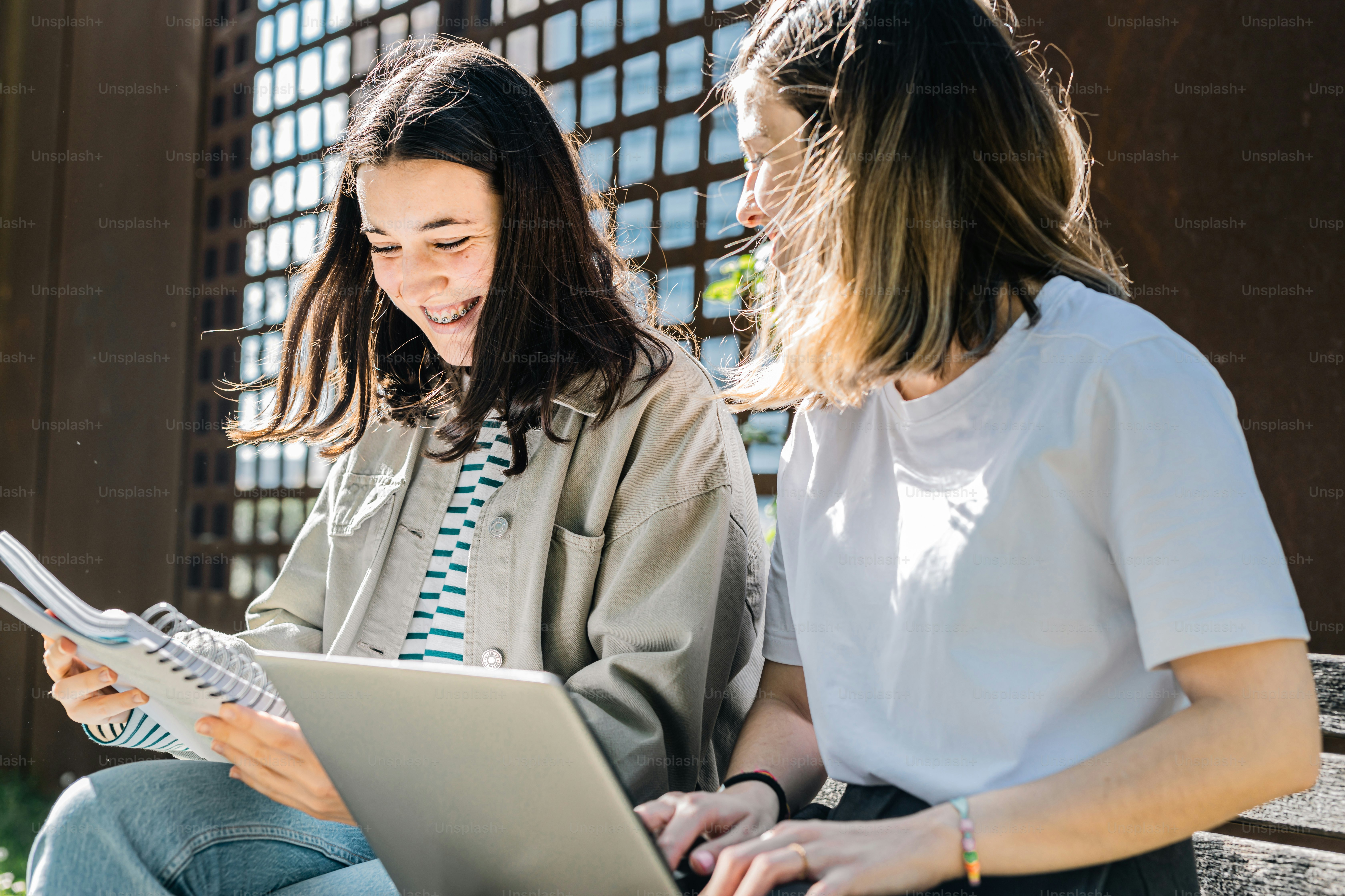 two women sitting on a bench looking at a laptop