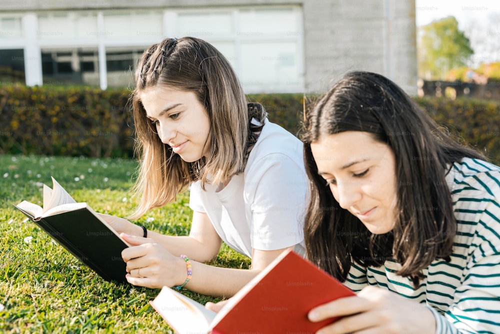 two girls laying on the grass reading books