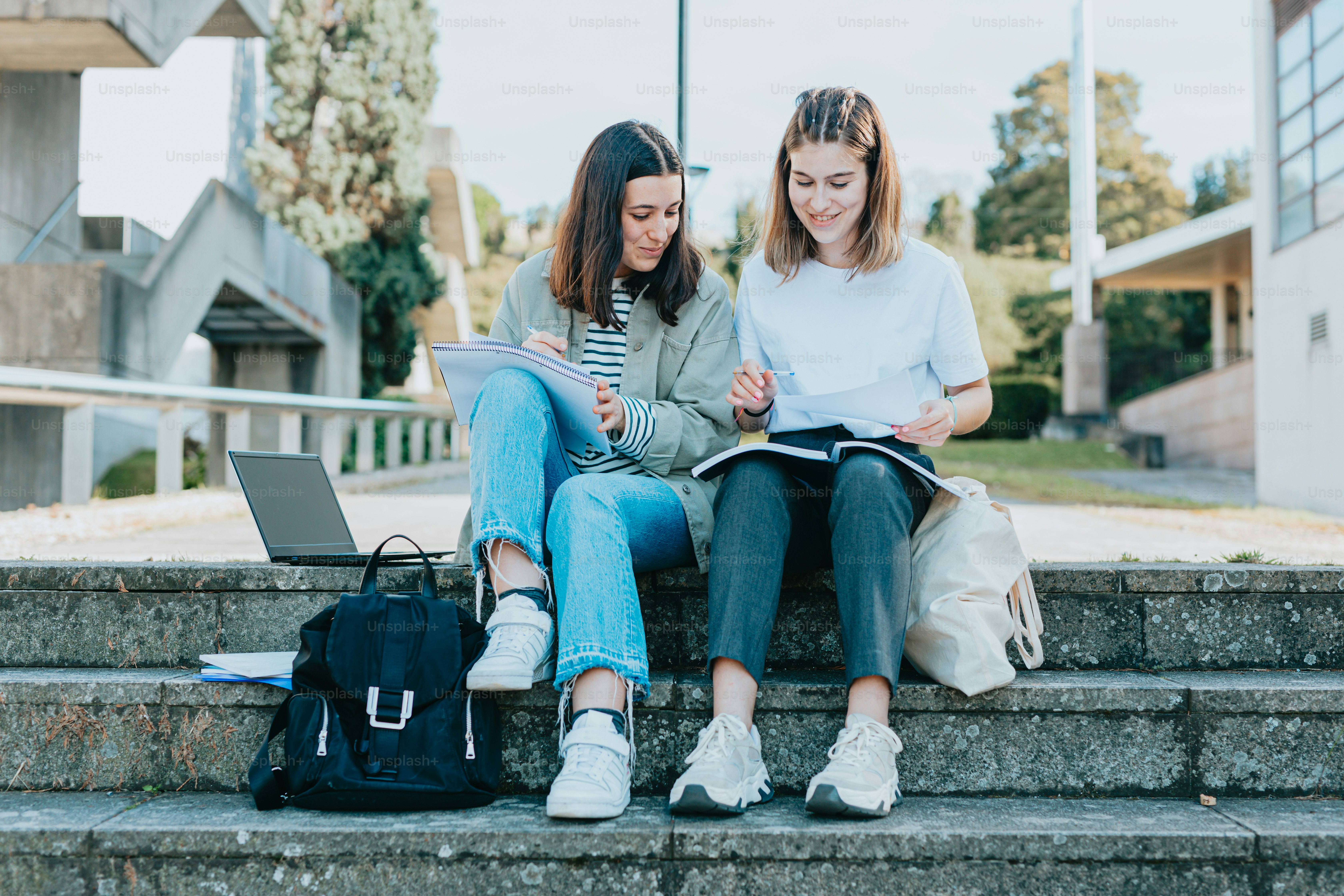 Dos mujeres jóvenes sentadas en escalones leyendo libros