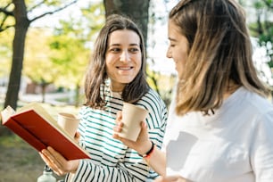 two women talking while holding coffee cups and books