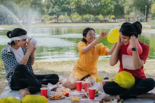 a group of women sitting on top of a field next to a lake