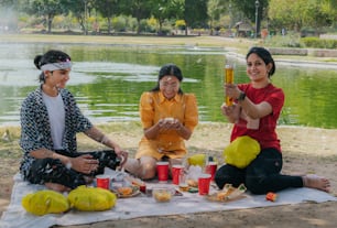 a group of women sitting on top of a blanket next to a lake