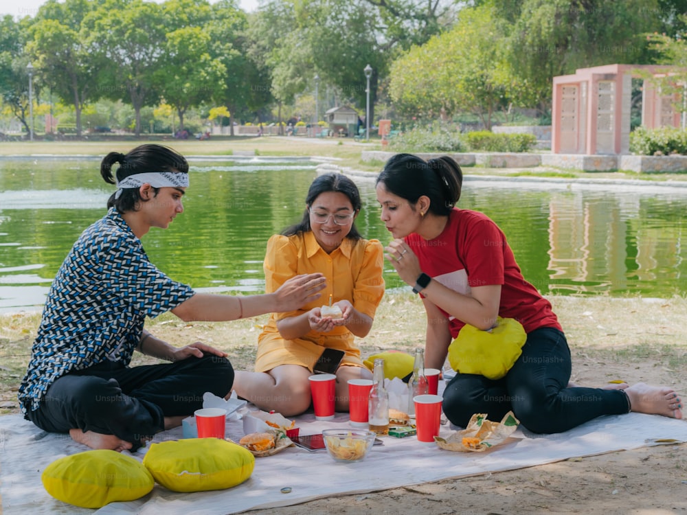 a group of people sitting on a blanket near a body of water