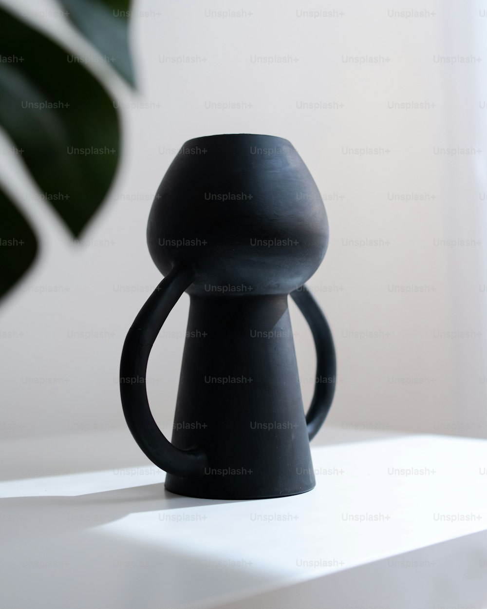 eine schwarze Vase, die auf einem weißen Tisch sitzt