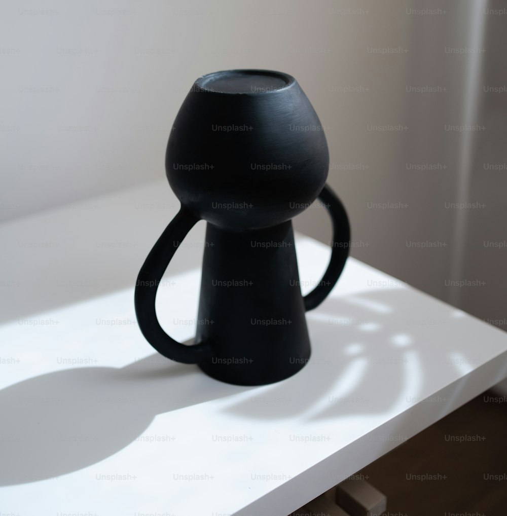 a black vase sitting on top of a white table