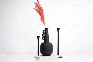 a black vase with a red flower in it