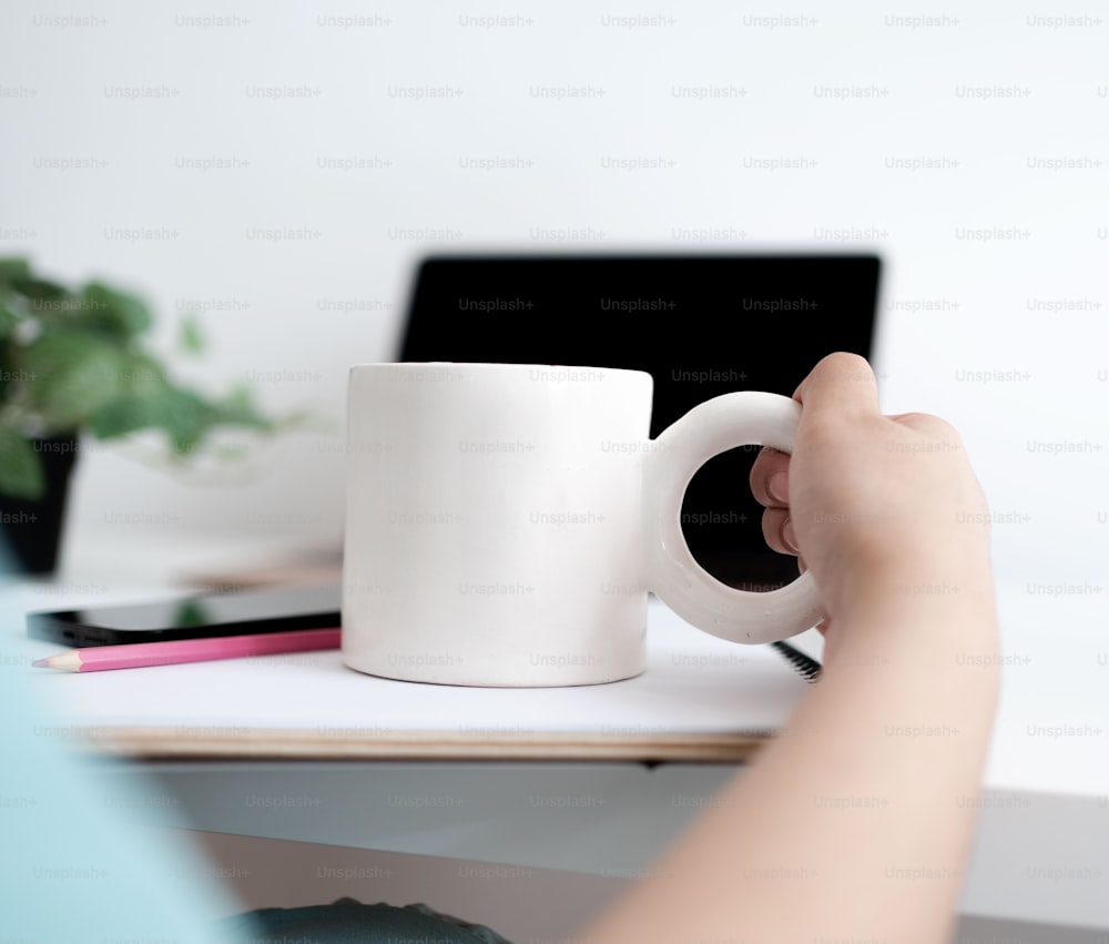 Una persona sosteniendo una taza de café frente a una computadora portátil