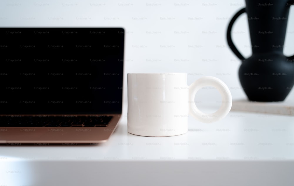 a white coffee mug sitting next to a laptop computer