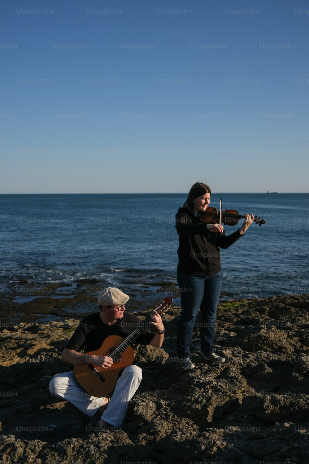 a man playing a violin and a woman playing a guitar on the beach