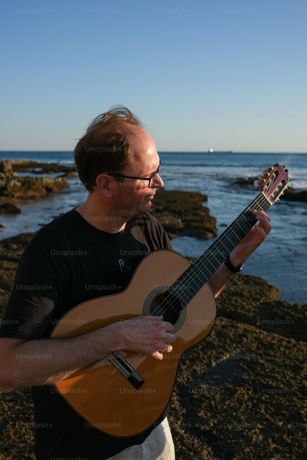 a man holding a guitar near the ocean