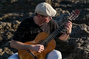 um homem sentado em uma rocha tocando uma guitarra