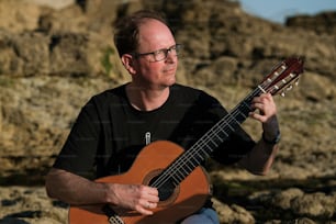 a man sitting on a rock playing a guitar