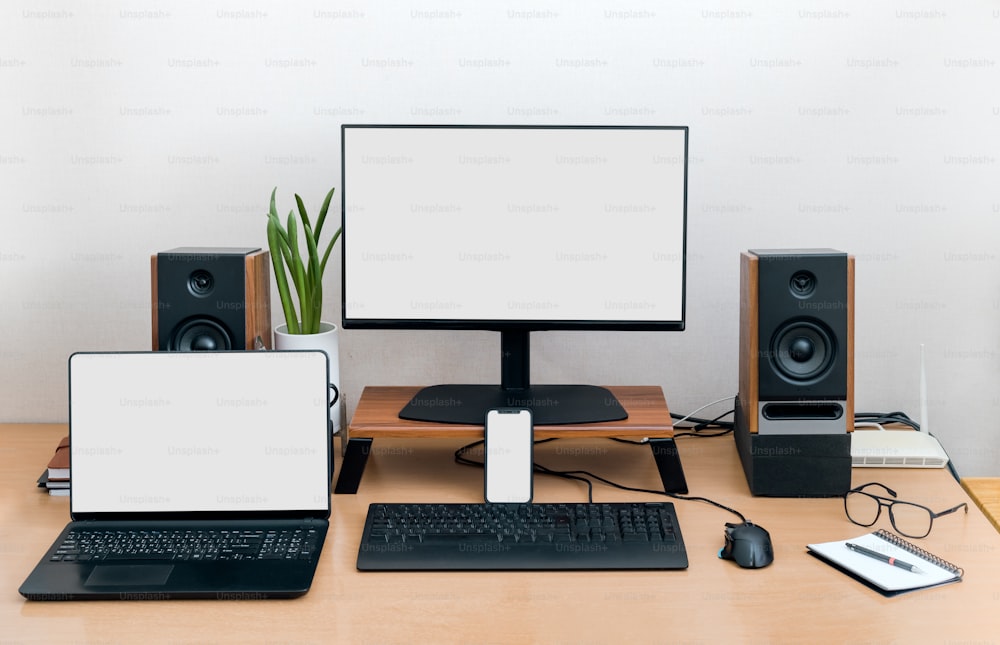 un escritorio con ordenador portátil, monitor, teclado y altavoces