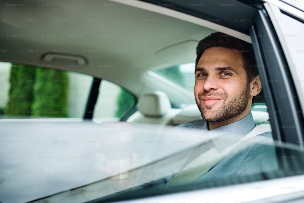 Young businessman with coffee sitting on back seat in car.