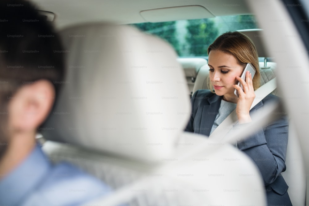 Business woman with smartphone sitting on back seats in taxi car, talking on the phone.