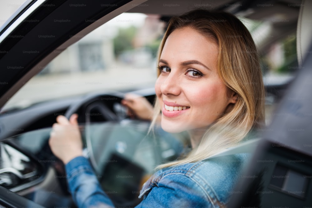 Motorista bonito da mulher jovem sentado no carro, olhando para fora.