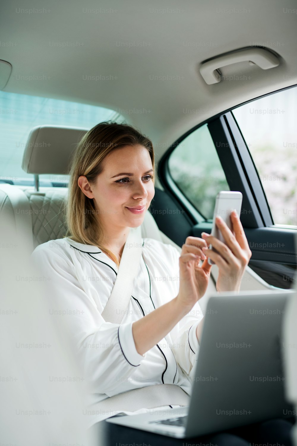 Uma empresária com laptop sentada no banco de trás do carro de táxi, tirando selfie.