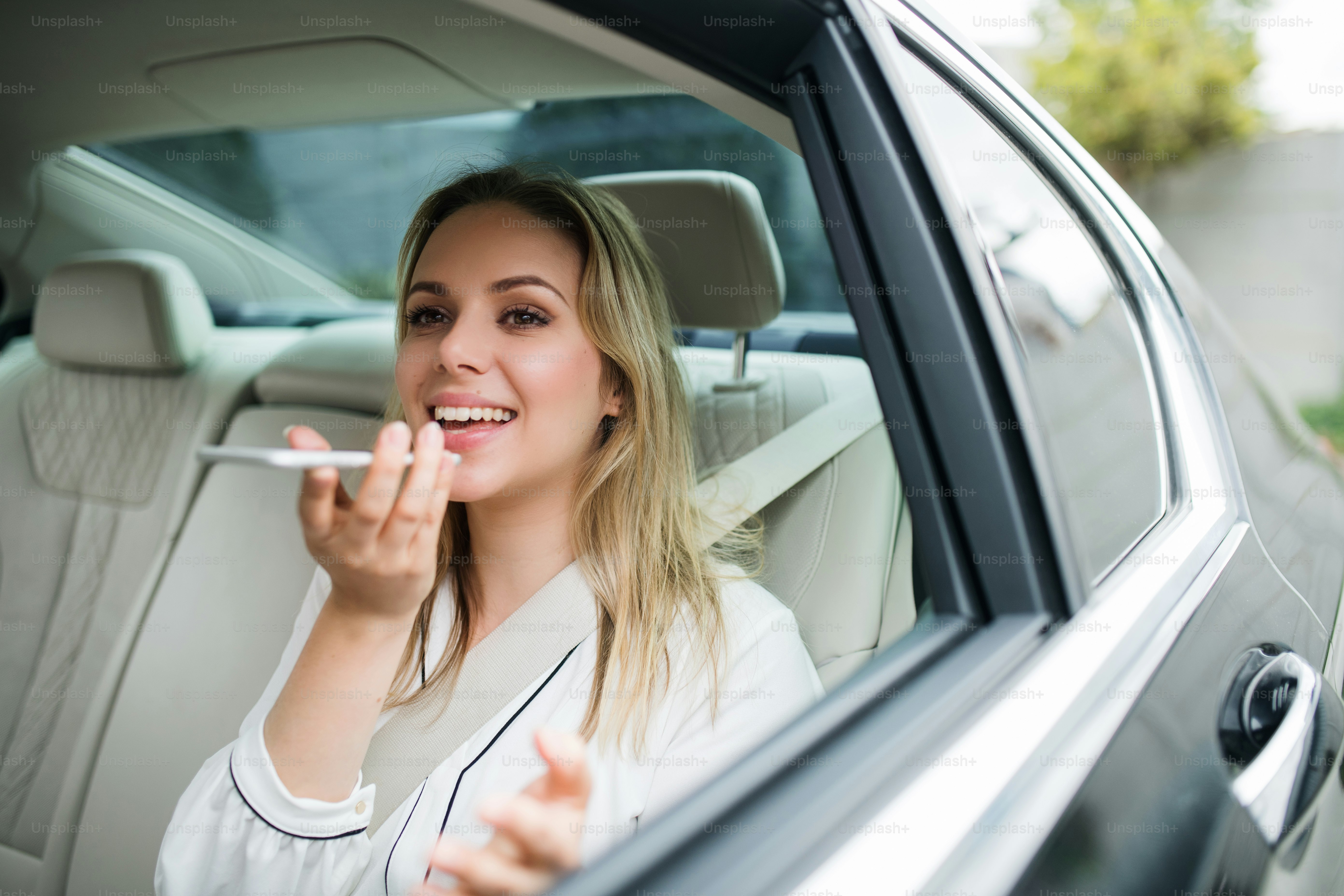 Mujer de negocios con teléfono inteligente y computadora portátil sentada en los asientos traseros en un taxi, hablando por teléfono.