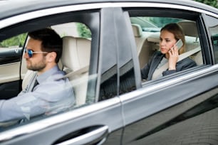 Femme d’affaires avec chauffeur assise sur le siège arrière dans une voiture de taxi, parlant au téléphone.