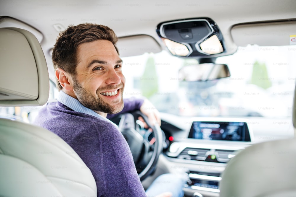 A businessman sitting in brand new car, looking back when driving.