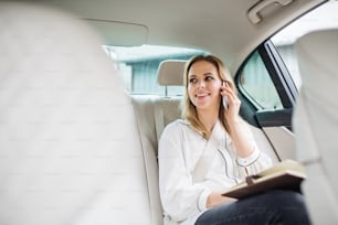タクシー車の後部座席に座り、電話で話すスマートフォンとノートパソコンを持つビジネスマン。