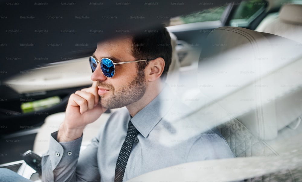 Un giovane uomo d'affari con occhiali da sole, camicia e cravatta seduto in auto.