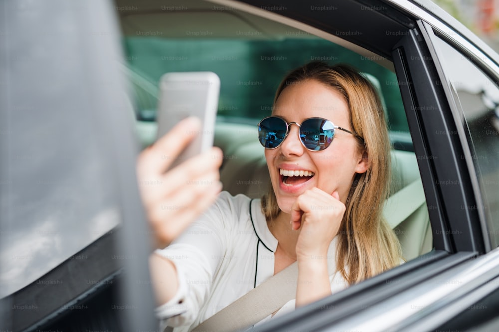Femme d’affaires assise sur le siège arrière dans une voiture de taxi, prenant un selfie. Espace de copie.