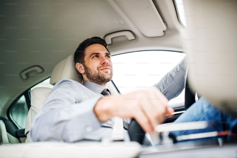 Young businessman with shirt and tie sitting in brand new car, driving.
