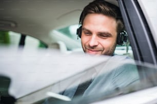 Young happy business man with headphones, shirt and tie sitting in car, listening to music.