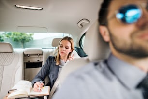 Mujer de negocios con teléfono inteligente sentada en el asiento trasero en un taxi, hablando por teléfono.