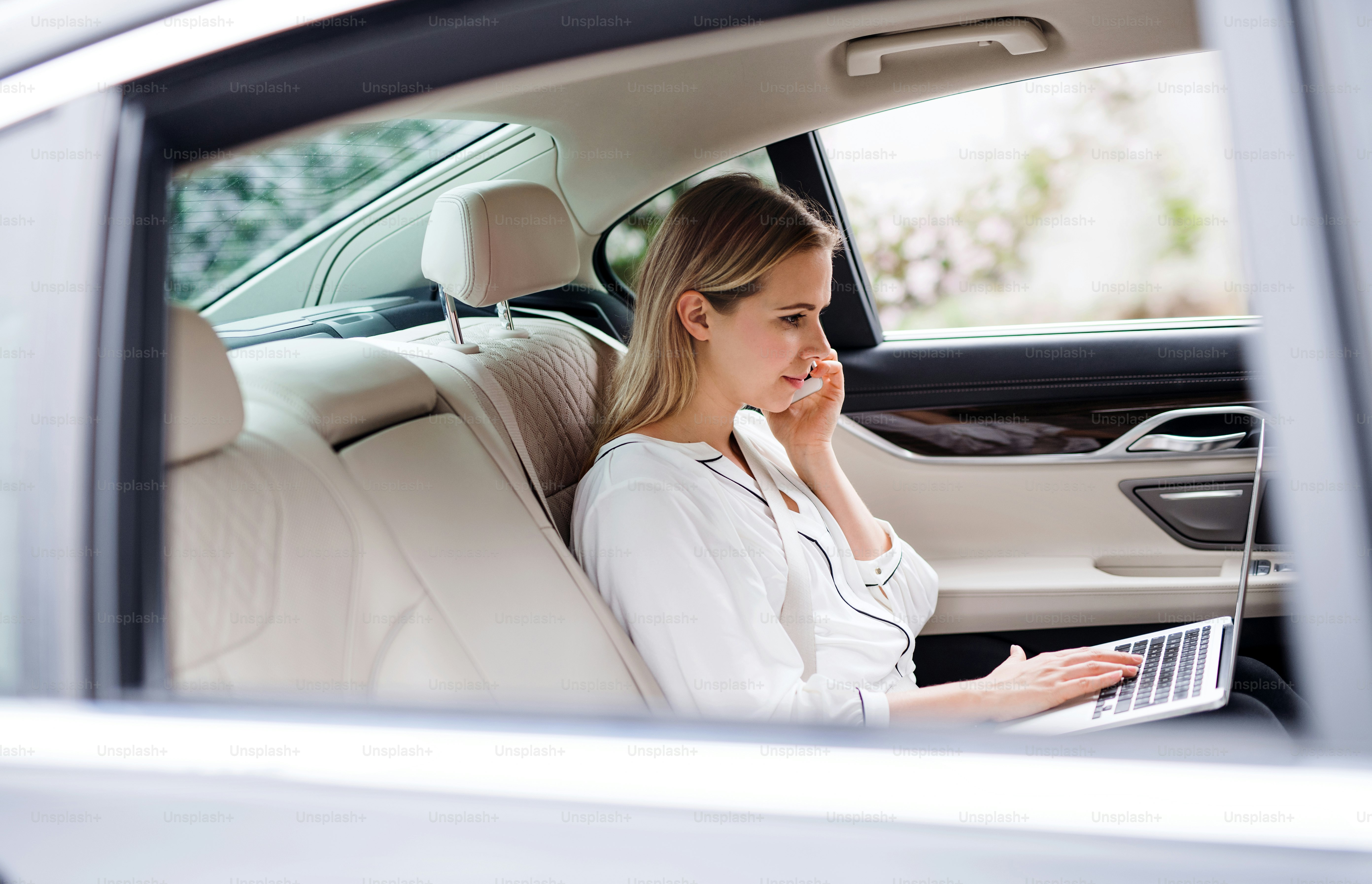 Mujer de negocios con teléfono inteligente y computadora portátil sentada en los asientos traseros en un taxi, hablando por teléfono.