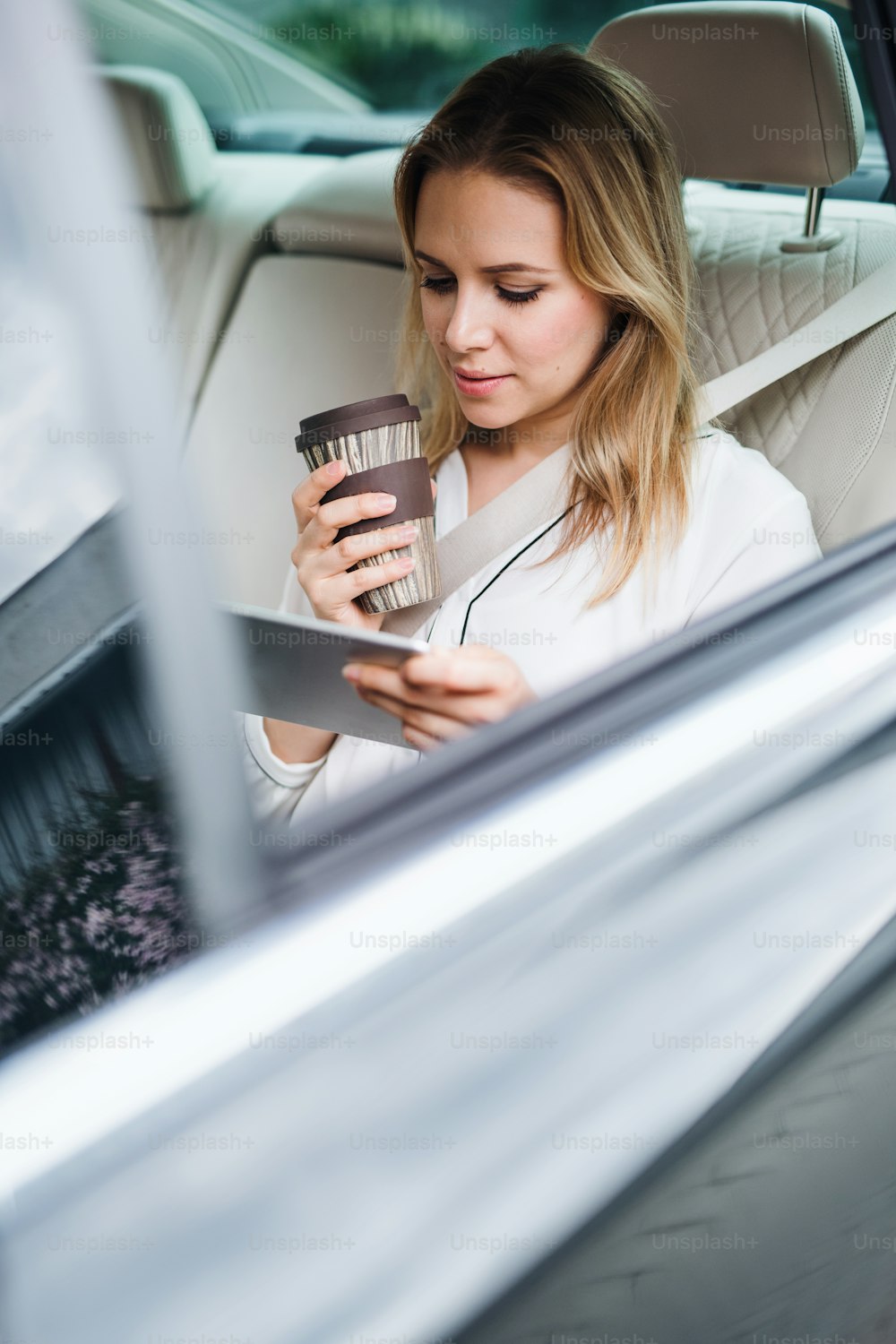 A business woman with tablet and coffee sitting on back seats in taxi car.