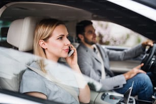 Una pareja joven feliz sentada en el coche, haciendo una llamada telefónica.