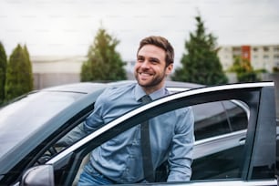 Happy young man with blue shirt and tie getting out of car in town.