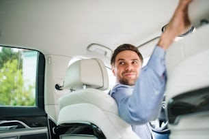 Um homem de negócios sentado em um carro novinho em folha, olhando para trás ao dirigir.