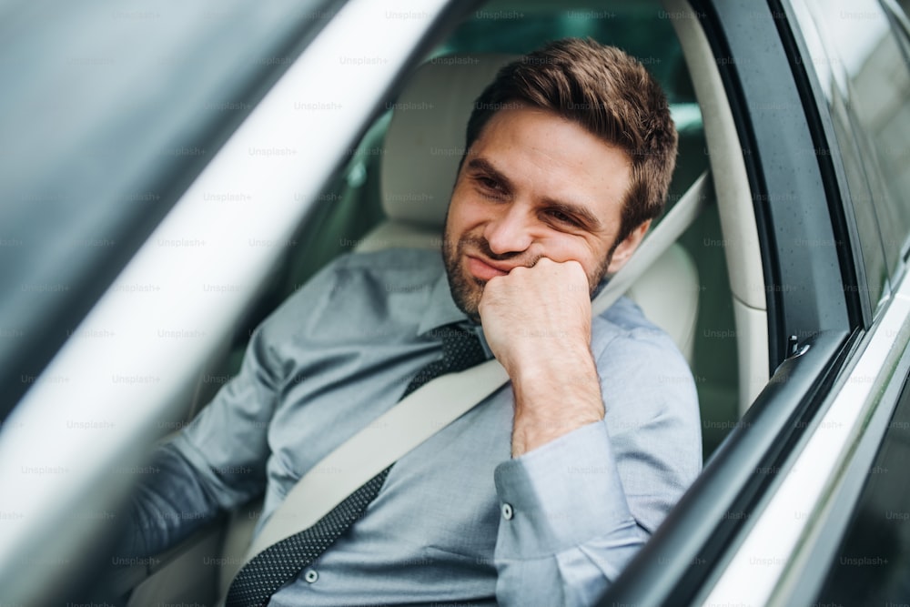Un giovane uomo d'affari annoiato con camicia e cravatta seduto in auto.