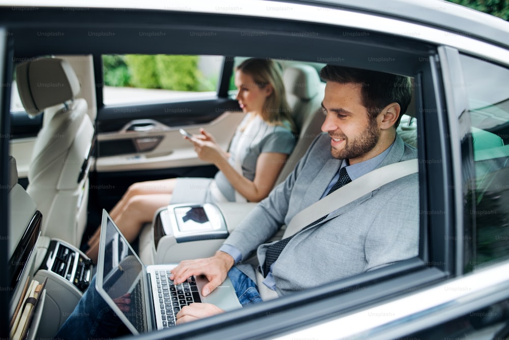 車の後部座席に座って働くノートパソコンを持つ若いビジネス夫婦。