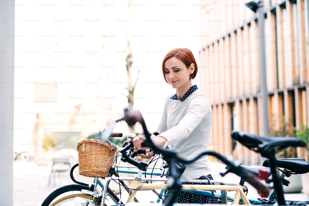 Um retrato de uma jovem mulher de negócios com bicicleta em pé ao ar livre.