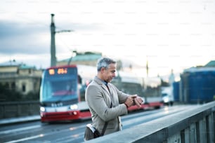 Bel homme d’affaires mature avec smartwatch debout sur un pont de la ville de Prague, vérifiant l’heure. Espace de copie.