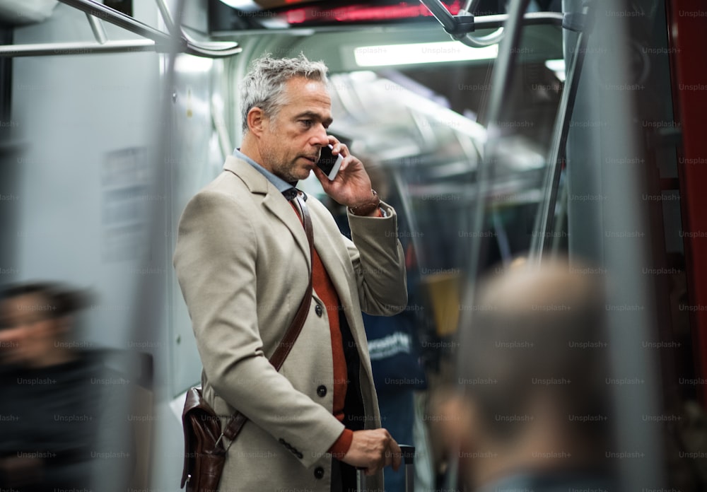 성숙한 잘생긴 사업가가 스마트폰을 들고 프라하 시내에서 지하철로 여행하며 전화를 걸고 있다.