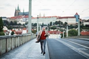 Reifer, gutaussehender Geschäftsmann mit Tasche, der auf einer Brücke in Prag spazieren geht und die Zeit überprüft. Speicherplatz kopieren.