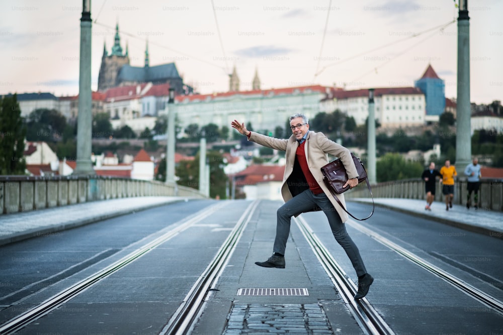 プラハ市の道路を横断するバッグを持つ幸せな成熟したハンサムなビジネスマン。