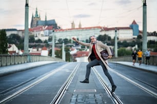 プラハ市の道路を横断するバッグを持つ幸せな成熟したハンサムなビジネスマン。