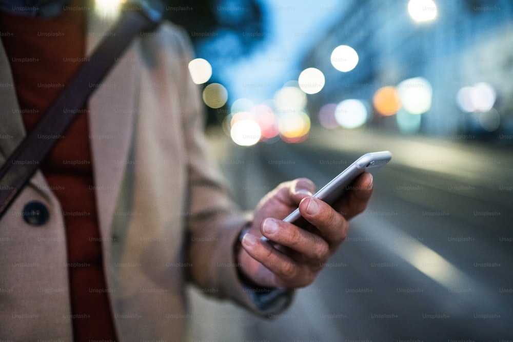 Eine Mittelteilansicht eines Geschäftsmannes mit Smartphone, der abends auf einer Straße steht. Eine Nahaufnahme.