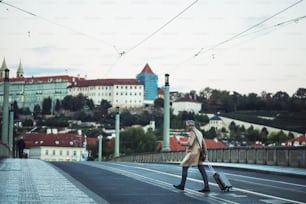 A mature businessman with smartphone and suitcase crossing a road in Prague city, text messaging.