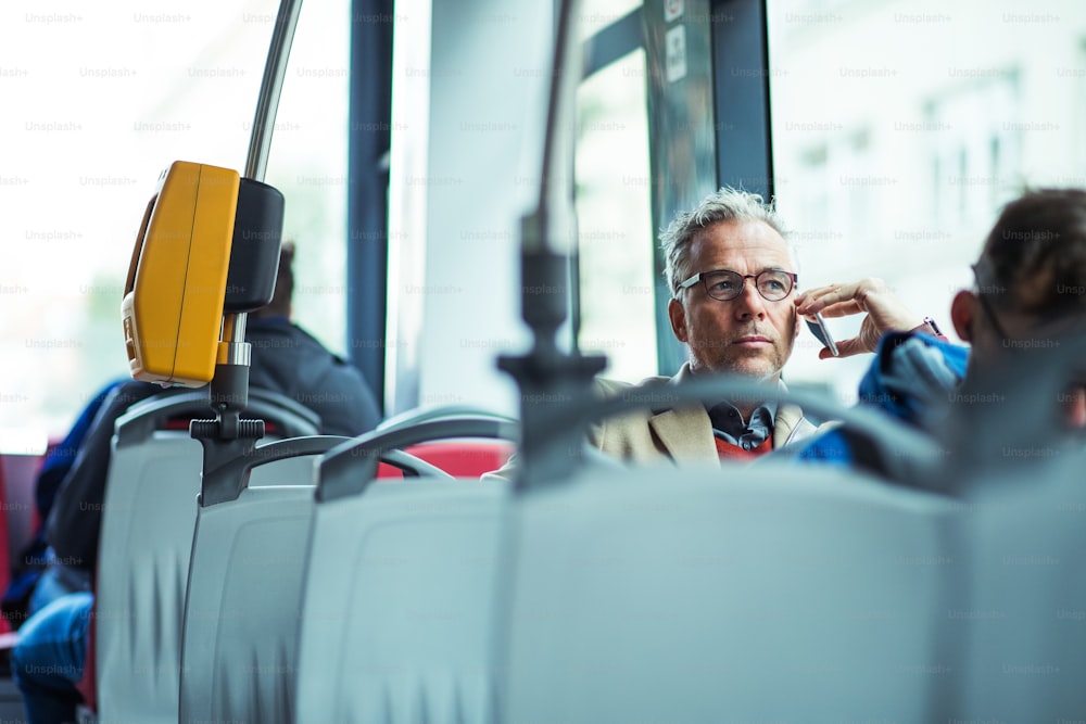 Hombre de negocios guapo maduro con teléfono inteligente que viaja en autobús en la ciudad, haciendo llamadas telefónicas. Espacio de copia.