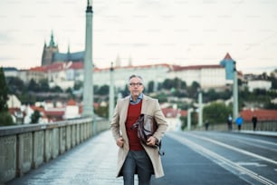Mature handsome businessman with bag walking on a bridge in Prague city. Copy space.